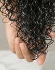 Hand holding a lock of curly black hair against a neutral background