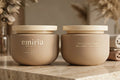 Two beige jars of emiria cream on a wooden surface with a blurred natural background.