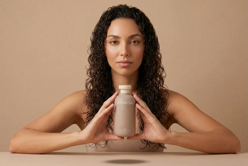 Woman holding a Emiria bottle against a beige background