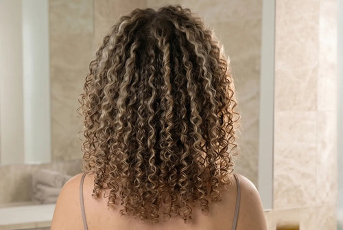 Person with curly hair standing in front of a bathroom mirror.