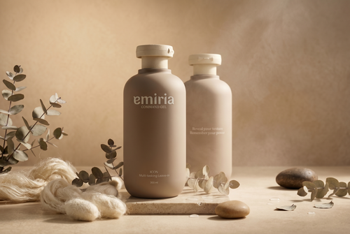 Two emria bottles on a neutral background with eucalyptus leaves and stones.